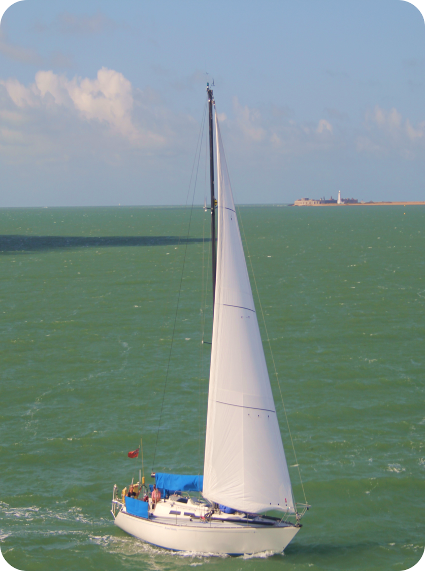 A yacht sailing on the Solent Water, with Hurst Point lighthouse in the background